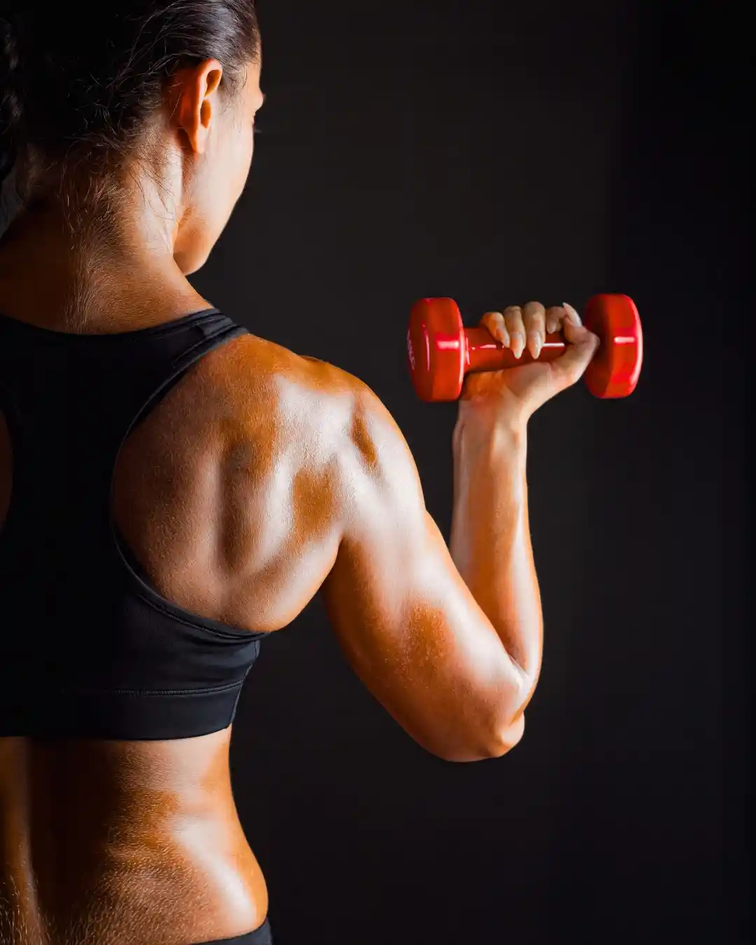Mujer entrenando con mancuerna roja, mostrando espalda y brazo definidos, ideal para fitness y fuerza femenina.